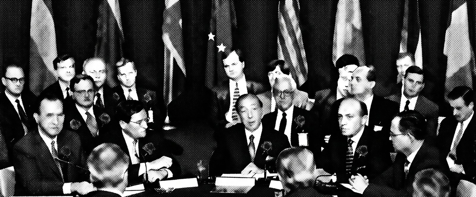 Photo d'archive : délégués réunis autour d'une table, drapeaux derrière eux.